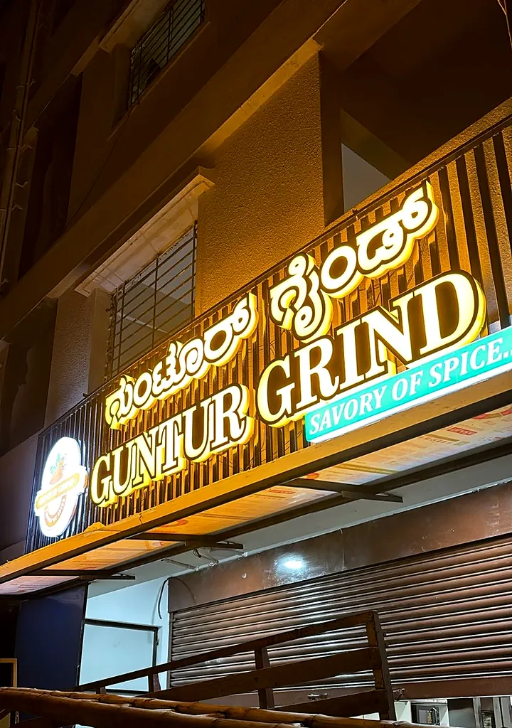 Guntur Grind fascia seen from below, gold letters glowing on a wooden slat facade