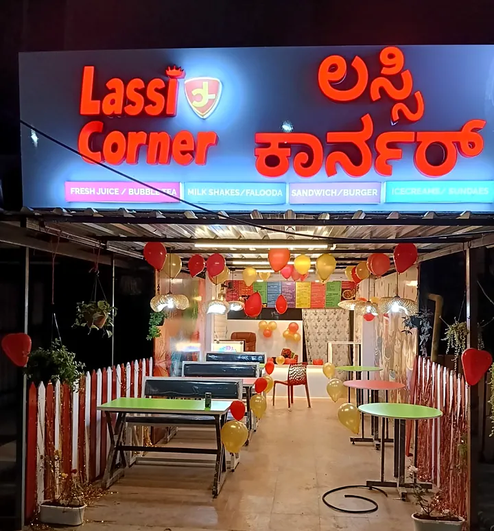 Lassi Corner outlet at night: red lit 3D letters in English and Kannada above a decorated seating area